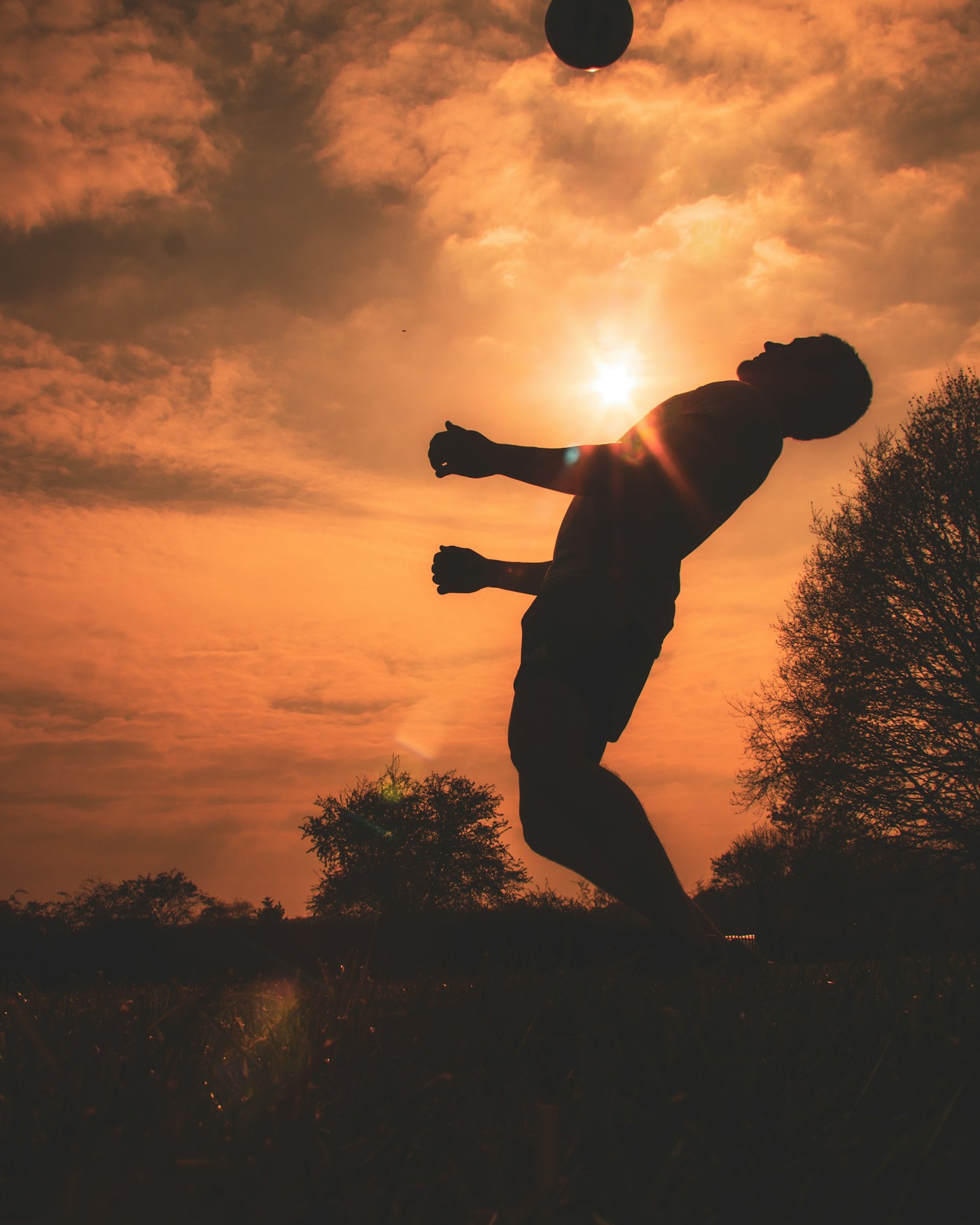 Silhouette of a soccer player performing a bicycle kick against a warm sunset sky