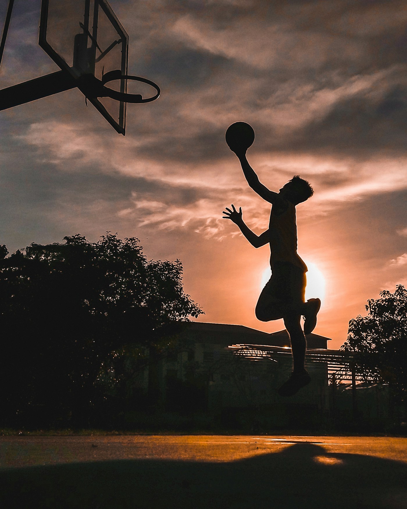 Silhouette of a basketball player mid-dunk against a golden sunset sky, hoop visible